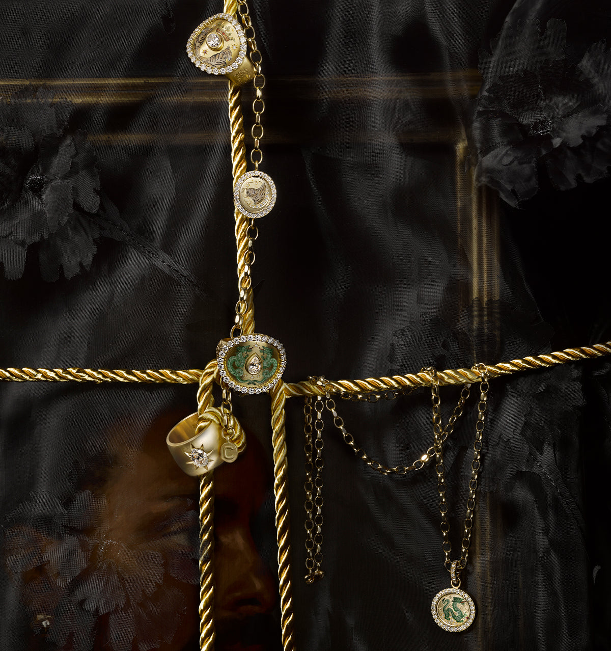 Gold chain featuring multiple pendants, including a green stone and intricate designs, displayed against a black backdrop.