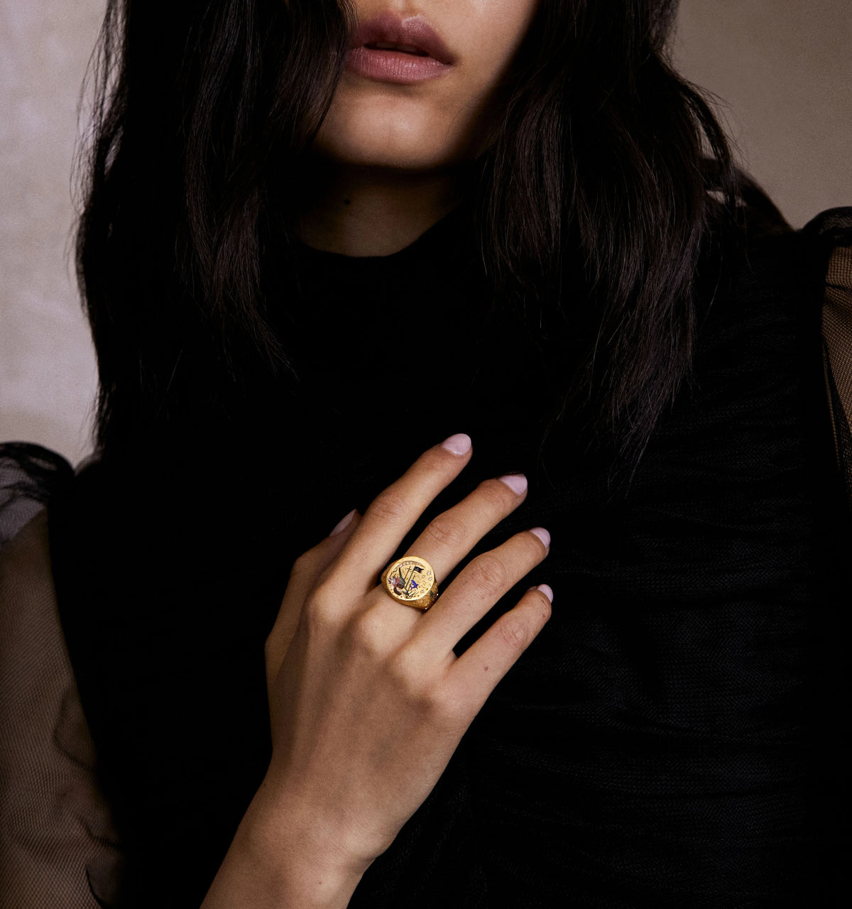 Woman wearing a gold ring with ocean motifs, set against a dark, textured background.