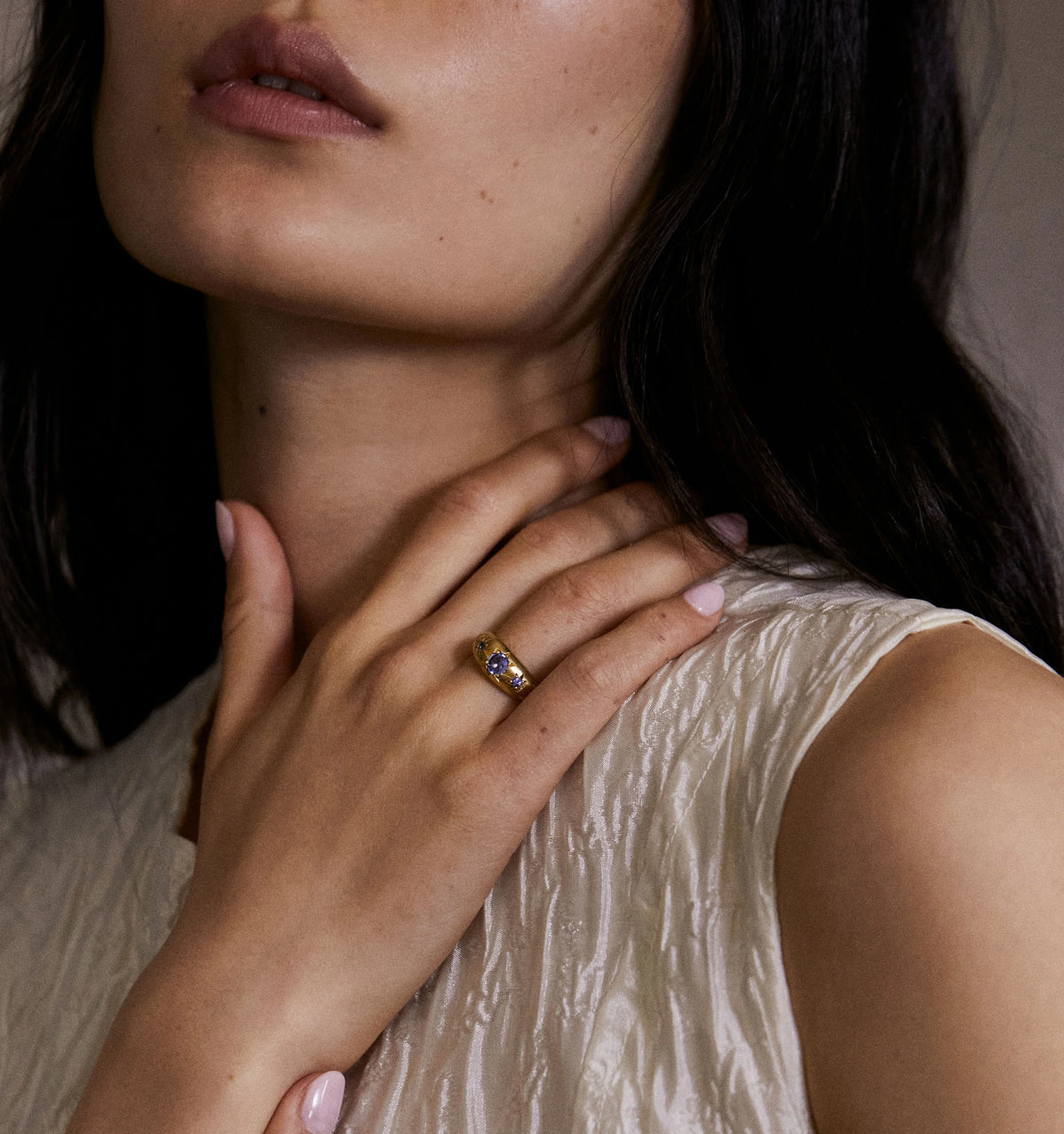 Woman wearing a gold ring featuring blue sapphires, photographed in soft lighting.