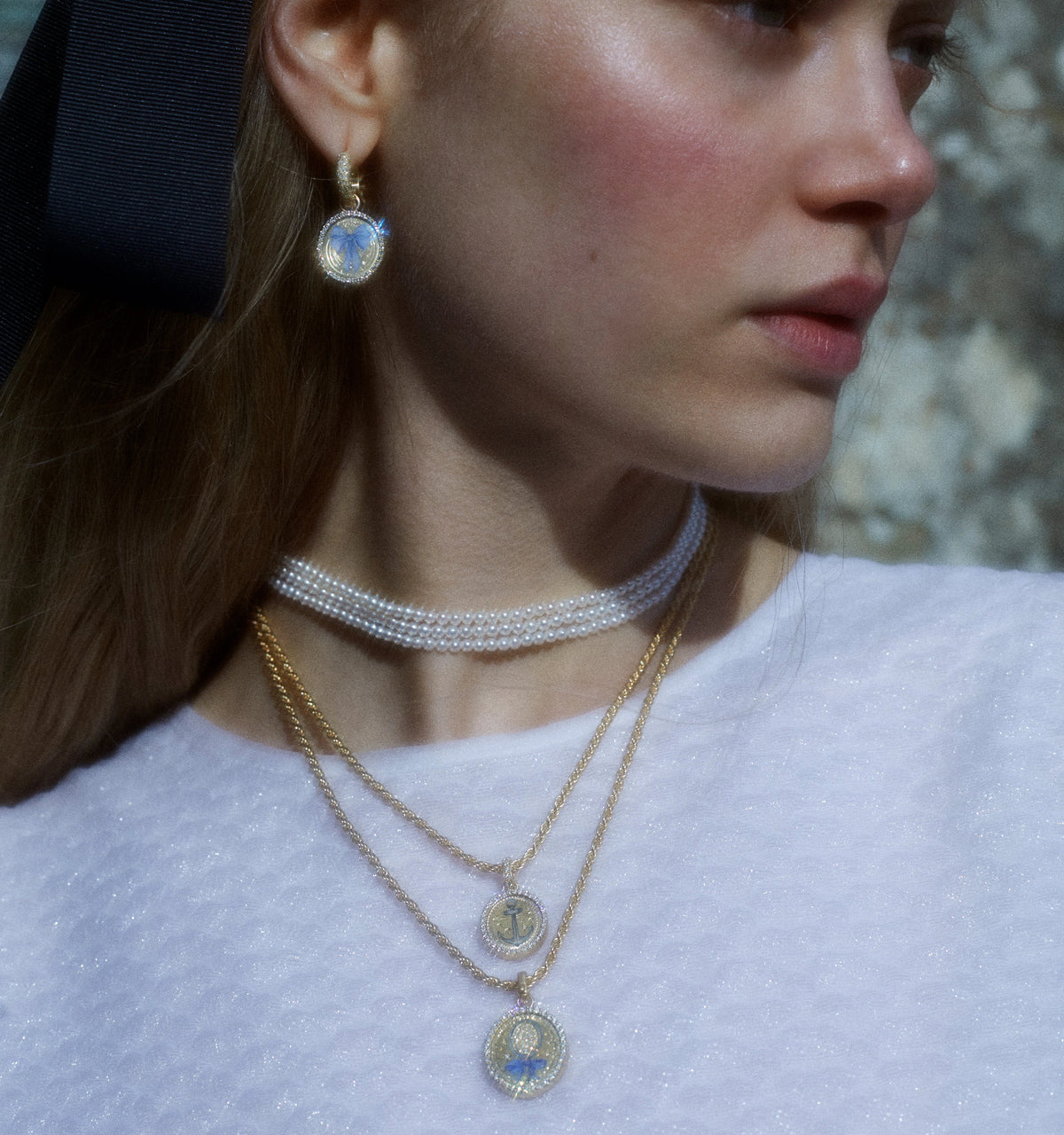 Woman wearing a gold pendant necklace with a blue enamel motif and gold hoop earrings.