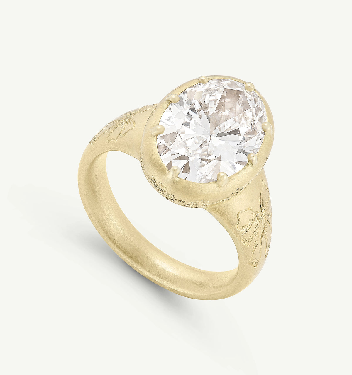 Gold ring featuring an oval, clear diamond set in a floral-engraved band.