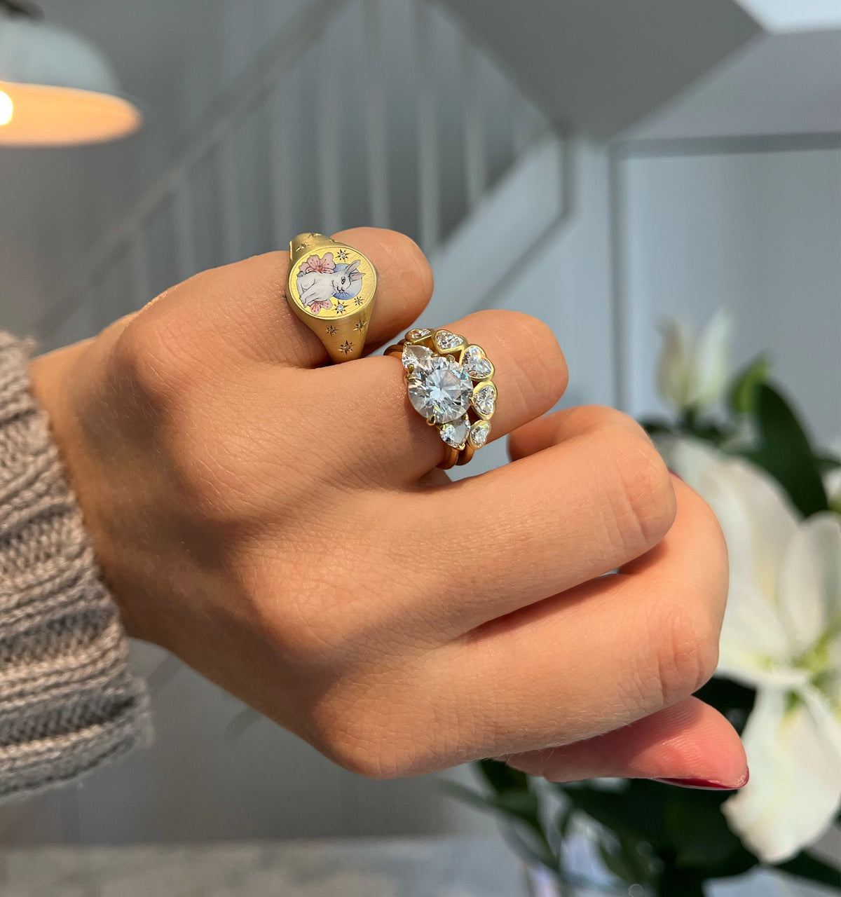 Woman wearing a gold ring with an enamel design alongside a gold ring featuring a large and small, surrounding diamonds.