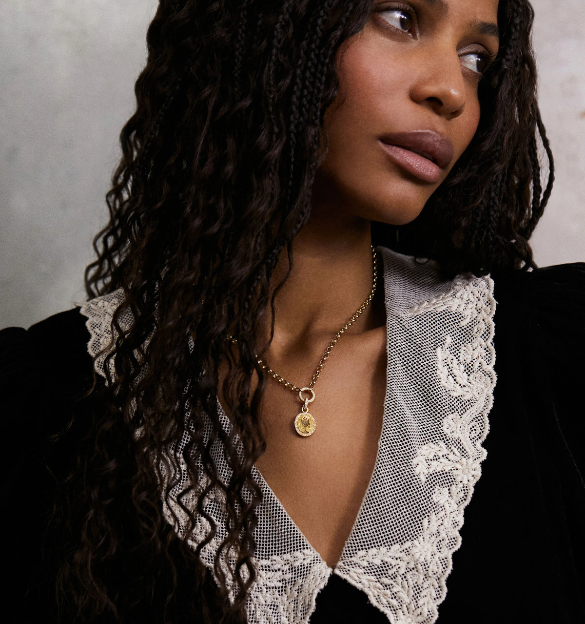 Woman wearing a gold pendant necklace with a detailed charm and a lace-trimmed blouse.