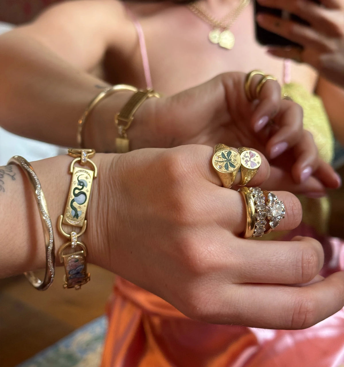 Woman wearing multiple gold rings and bracelets, including a gold bracelet with enamel detailing and a gold ring with diamonds.