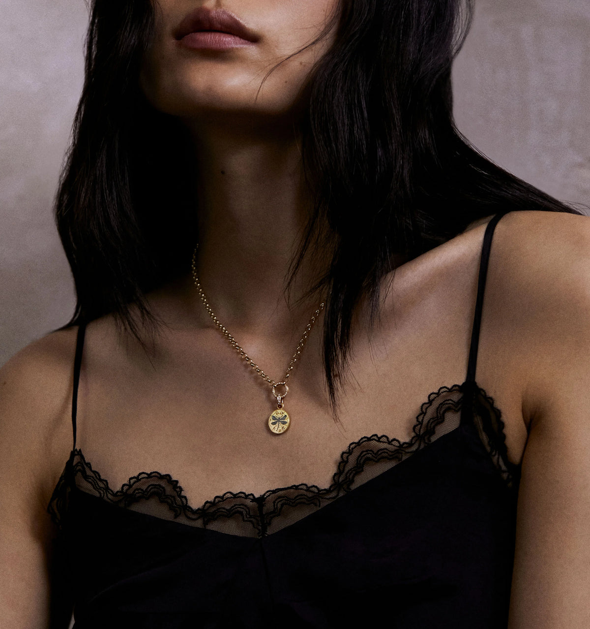 Woman wearing a gold pendant necklace with an intricate design, paired with a black lace top.