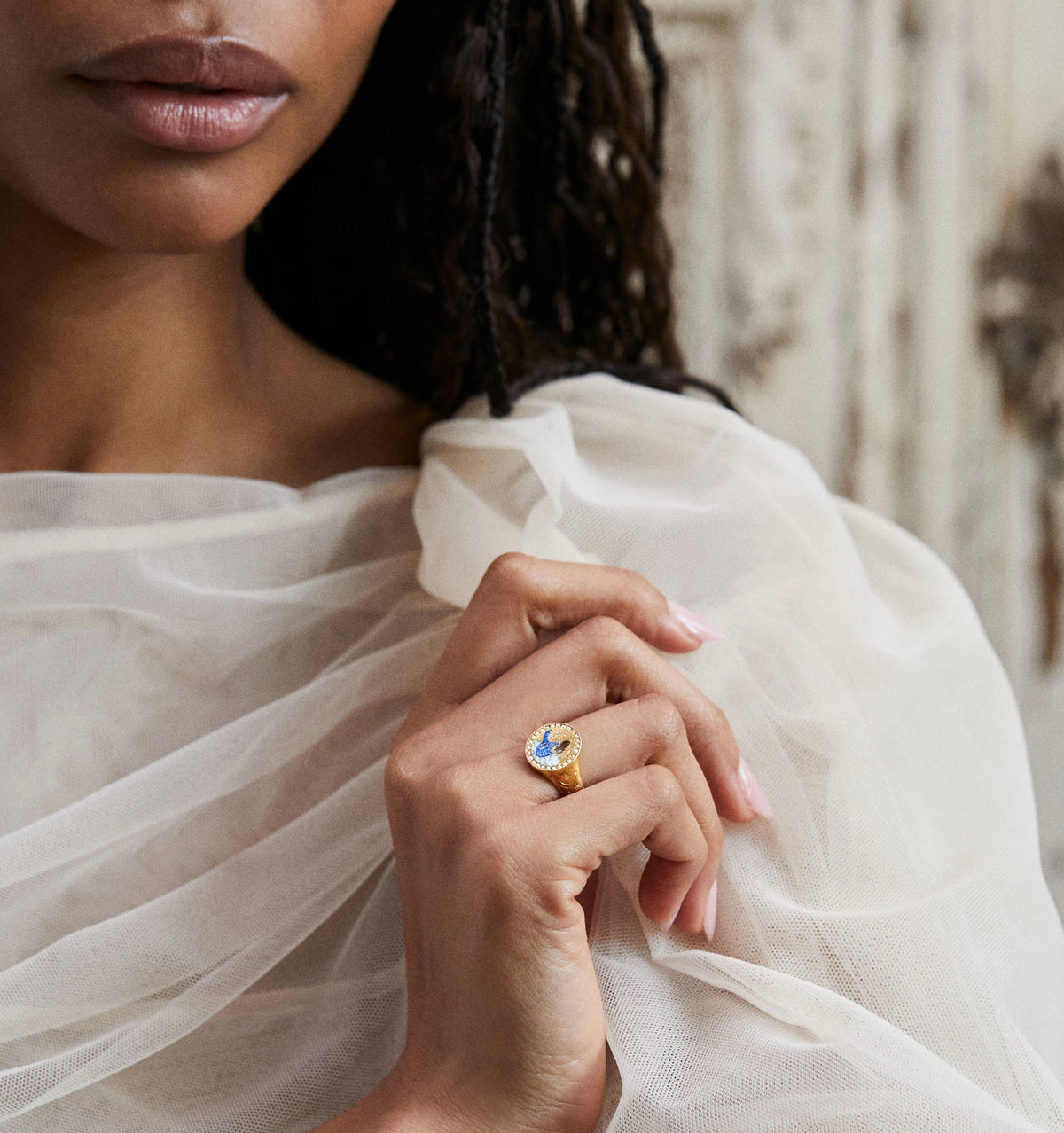 Woman wearing a gold ring featuring a blue stone surrounded by smaller diamonds.