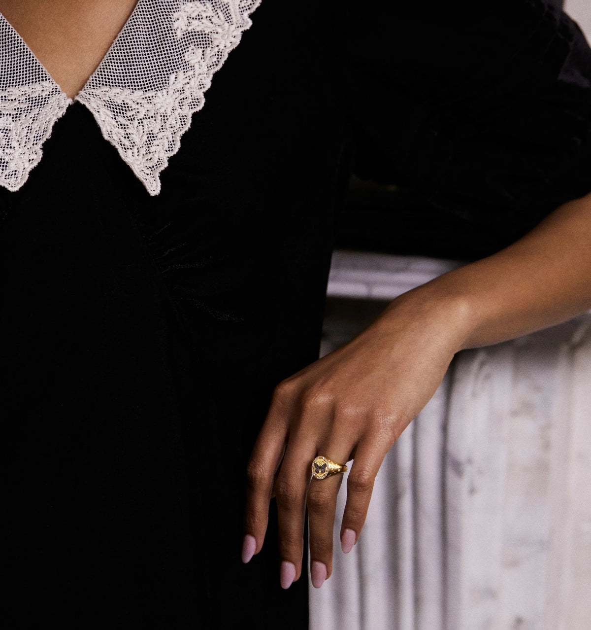 Woman wearing a gold ring with a heart design and a lace-collared black dress.