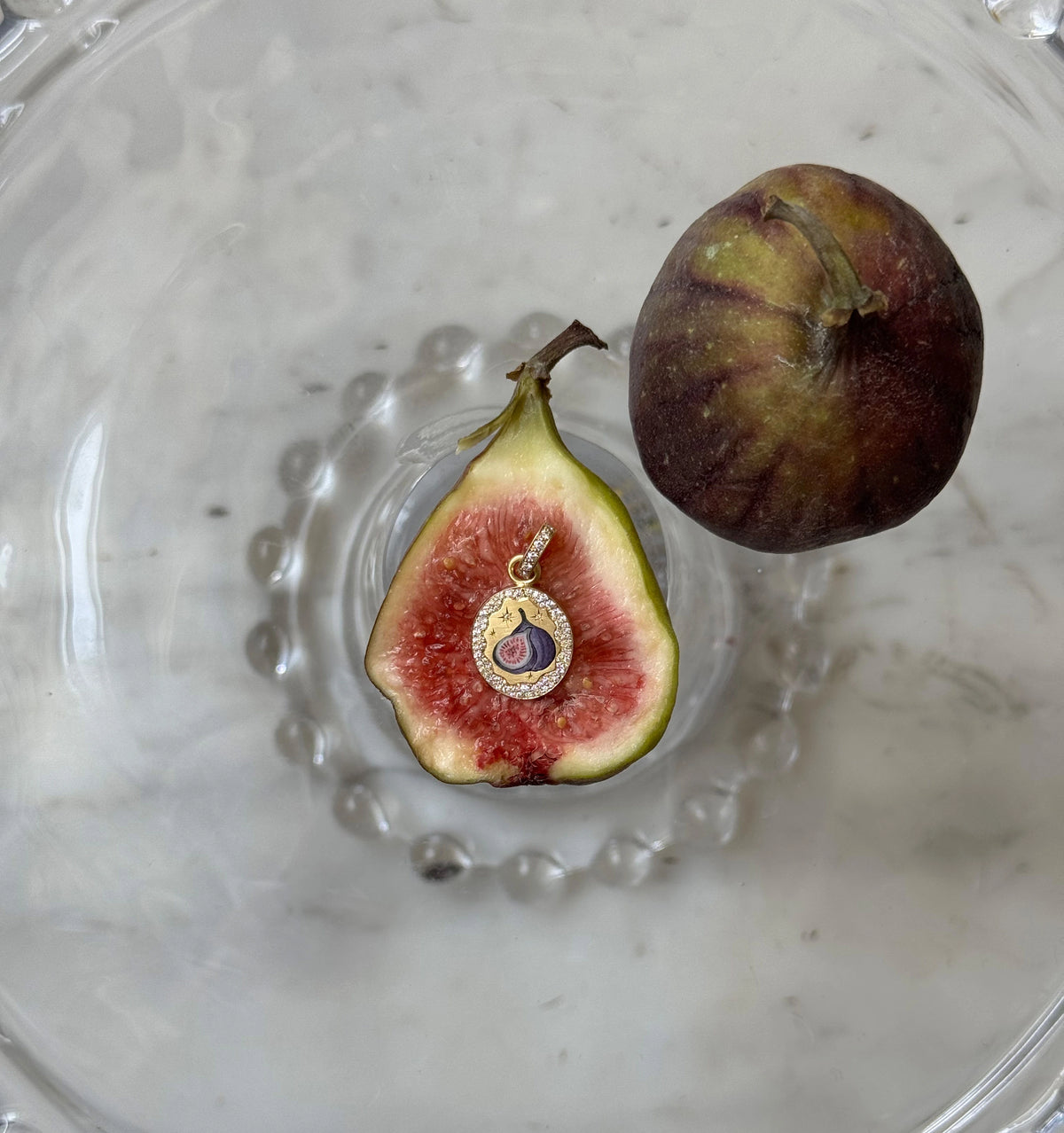 Gold pendant featuring a fig design with enamel and surrounding diamonds placed on a halved fig.
