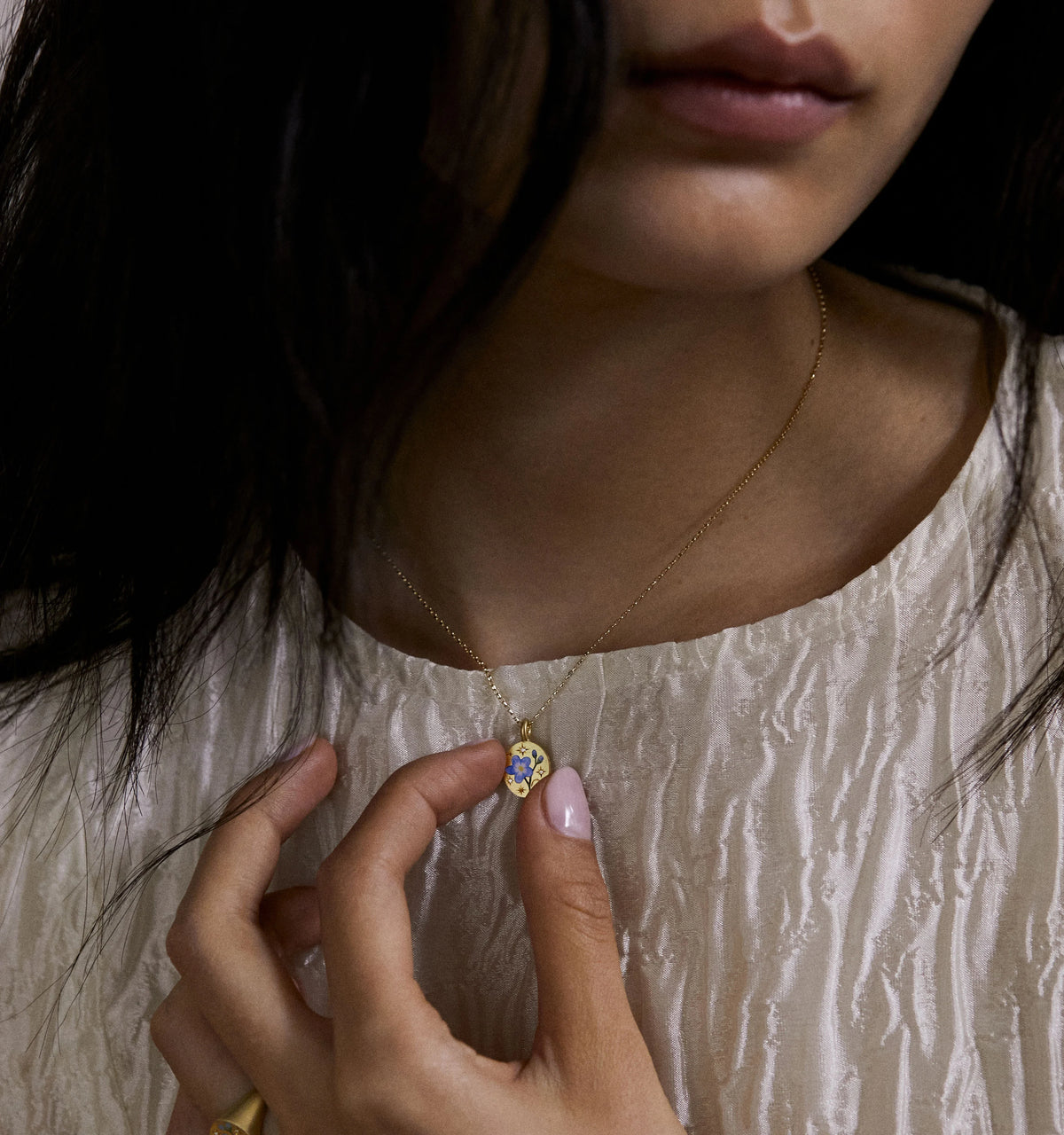Woman wearing a gold necklace with an enamel heart pendant, touching the pendant gently.