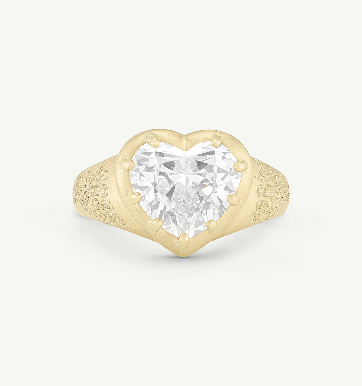 Heart-shaped gold ring featuring a large clear stone and intricate floral engravings on the band.