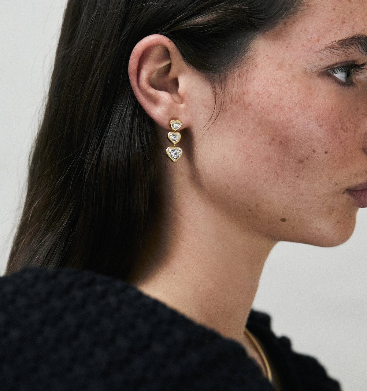 Woman wearing gold earrings with heart-shaped and round diamonds.
