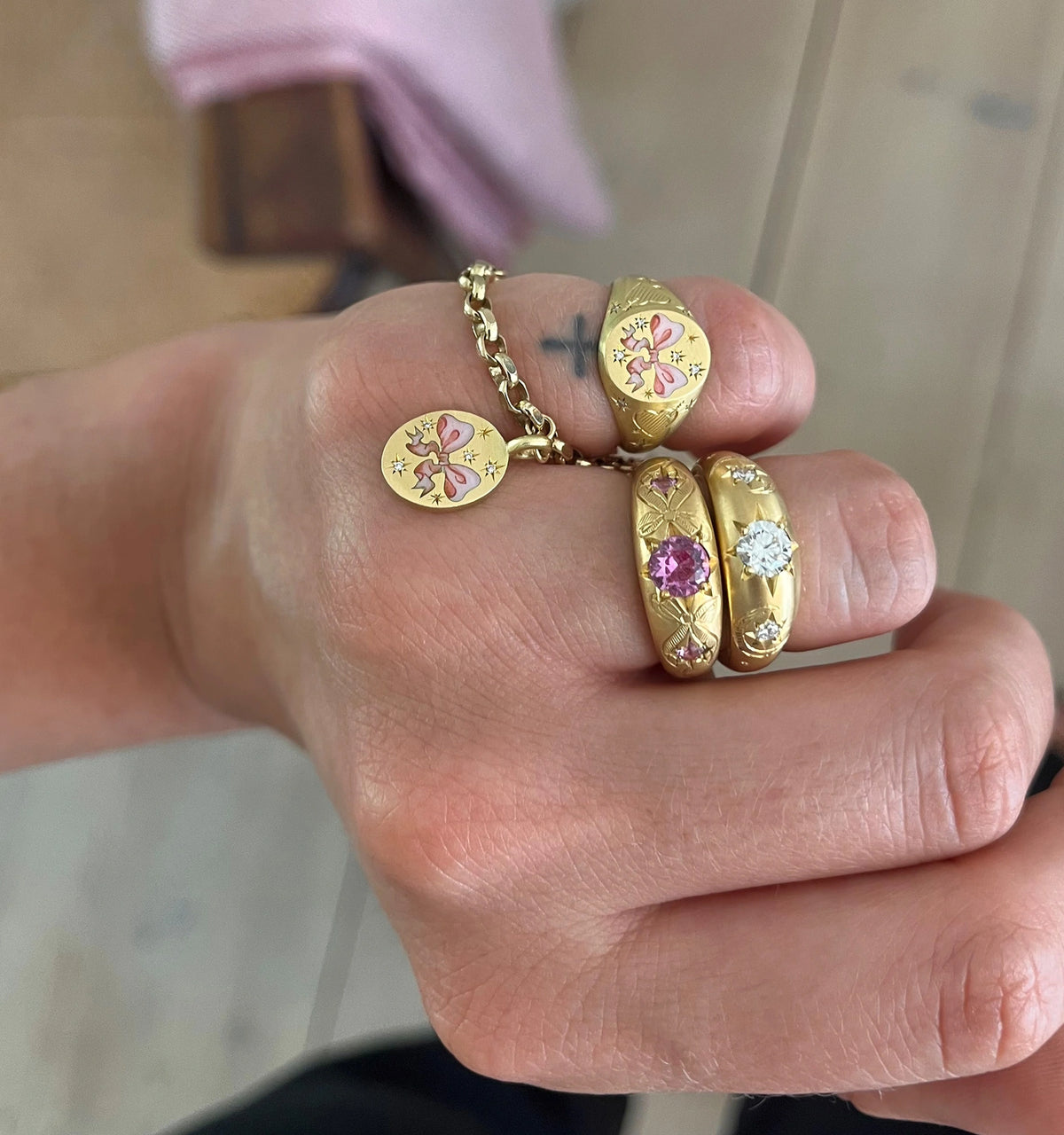 Woman wearing gold rings featuring pink sapphires and diamonds, along with a gold bracelet and pendant.