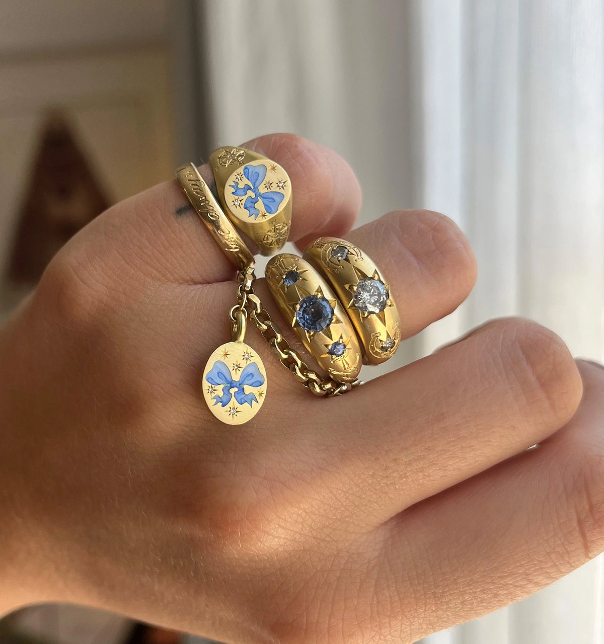 Woman wearing a stack of gold rings featuring blue enamel, and one with a blue stone hanging from a chain.