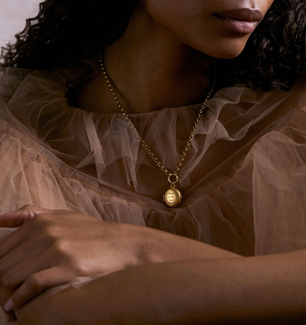 Woman wearing a gold pendant necklace on a delicate chain, with a sheer, ruffled top.