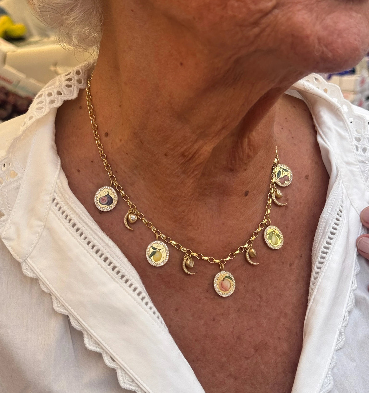 Woman wearing a gold necklace with colourful enamel charms and crescent moon accents.