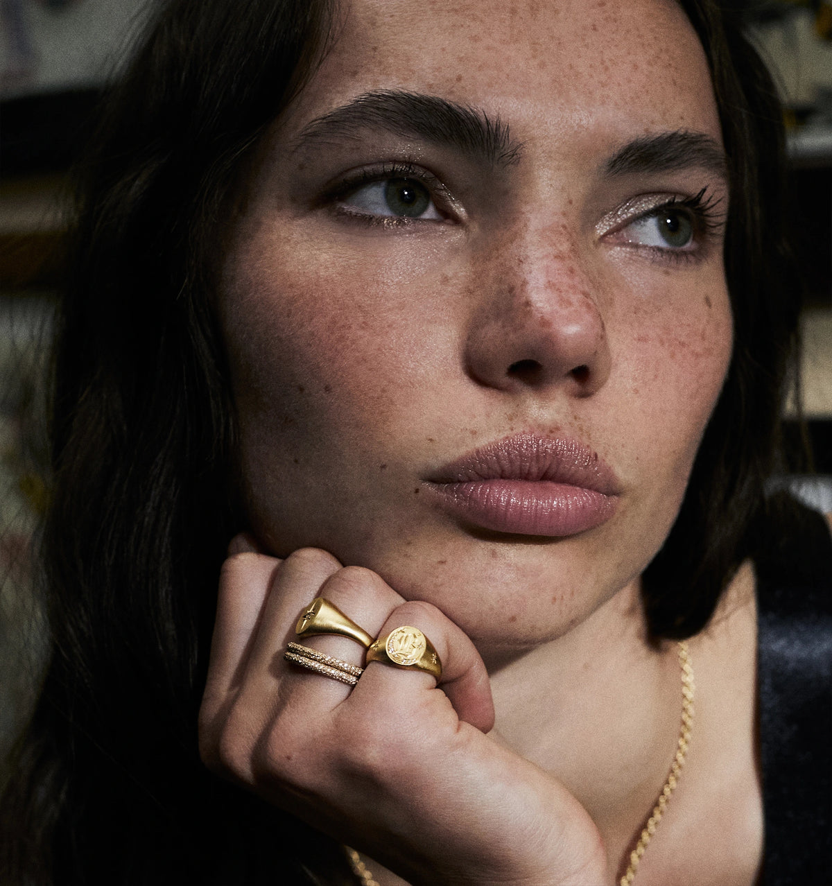 Woman wearing multiple gold rings, including a smooth band and a ring with an engraved design.