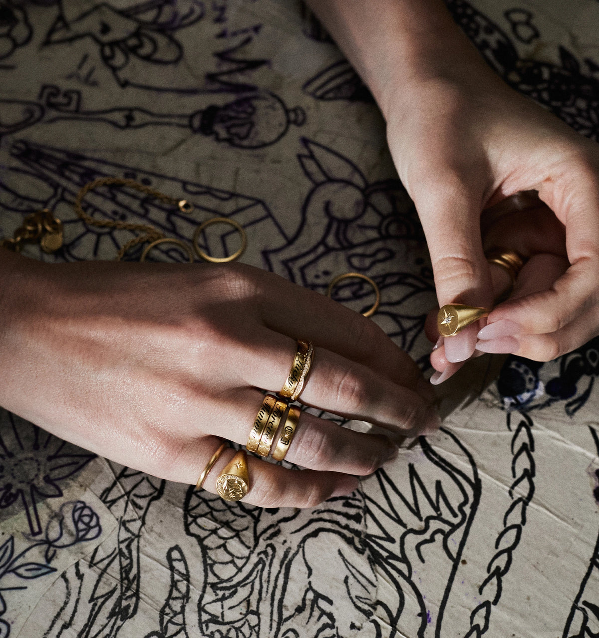 Woman wearing multiple gold rings, including a signet ring with a star design, against a patterned surface.