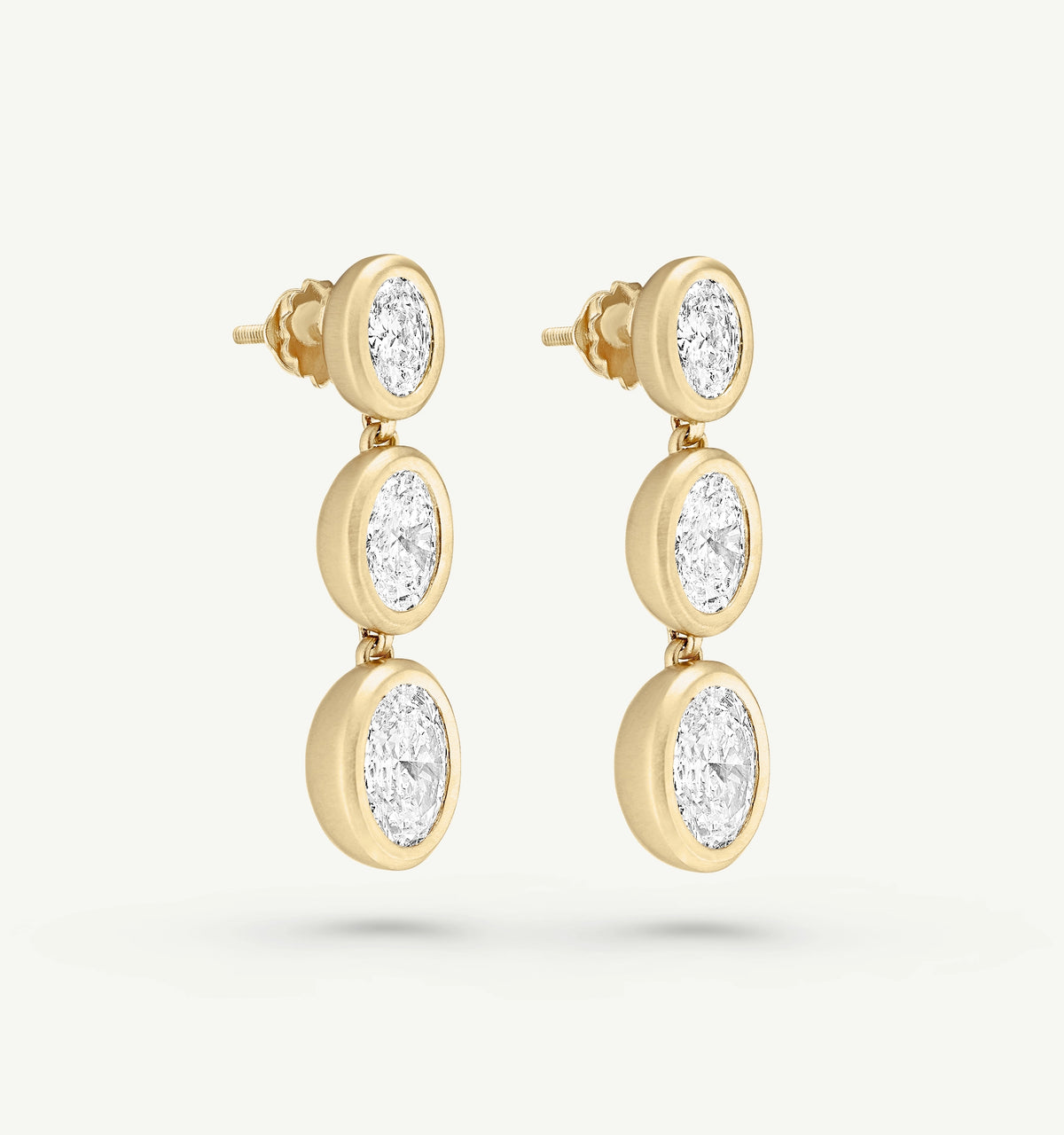 Gold drop earrings featuring three oval clear diamonds set in a polished gold backdrop.