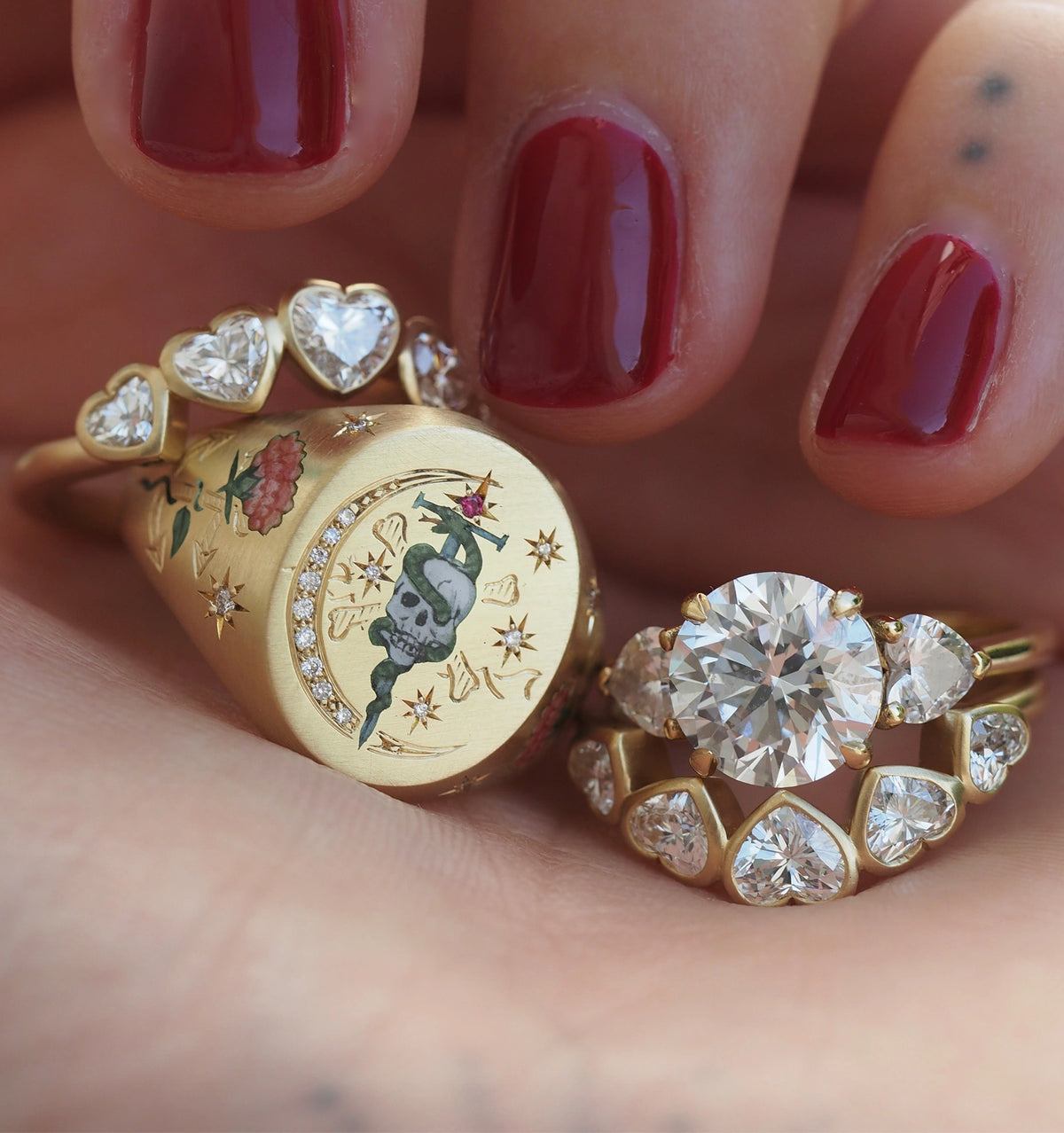 Woman wearing a gold ring with floral and skull motifs, alongside a gold ring featuring multiple round diamonds.