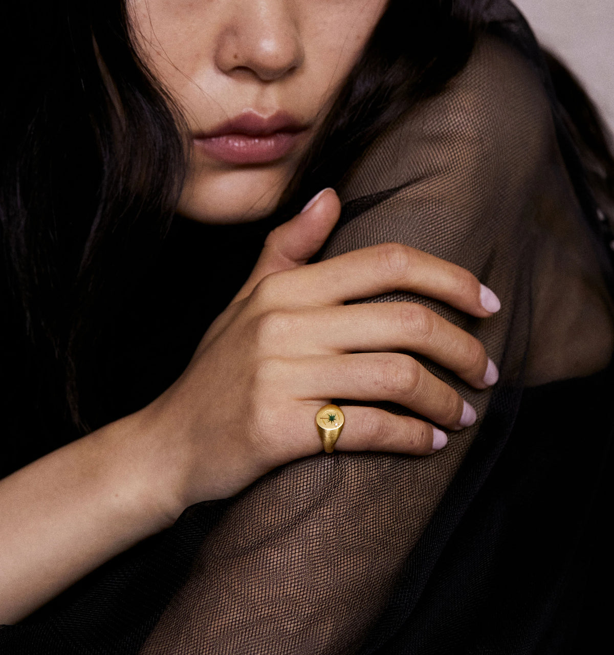 Woman wearing a gold ring featuring a green stone in a textured black top.