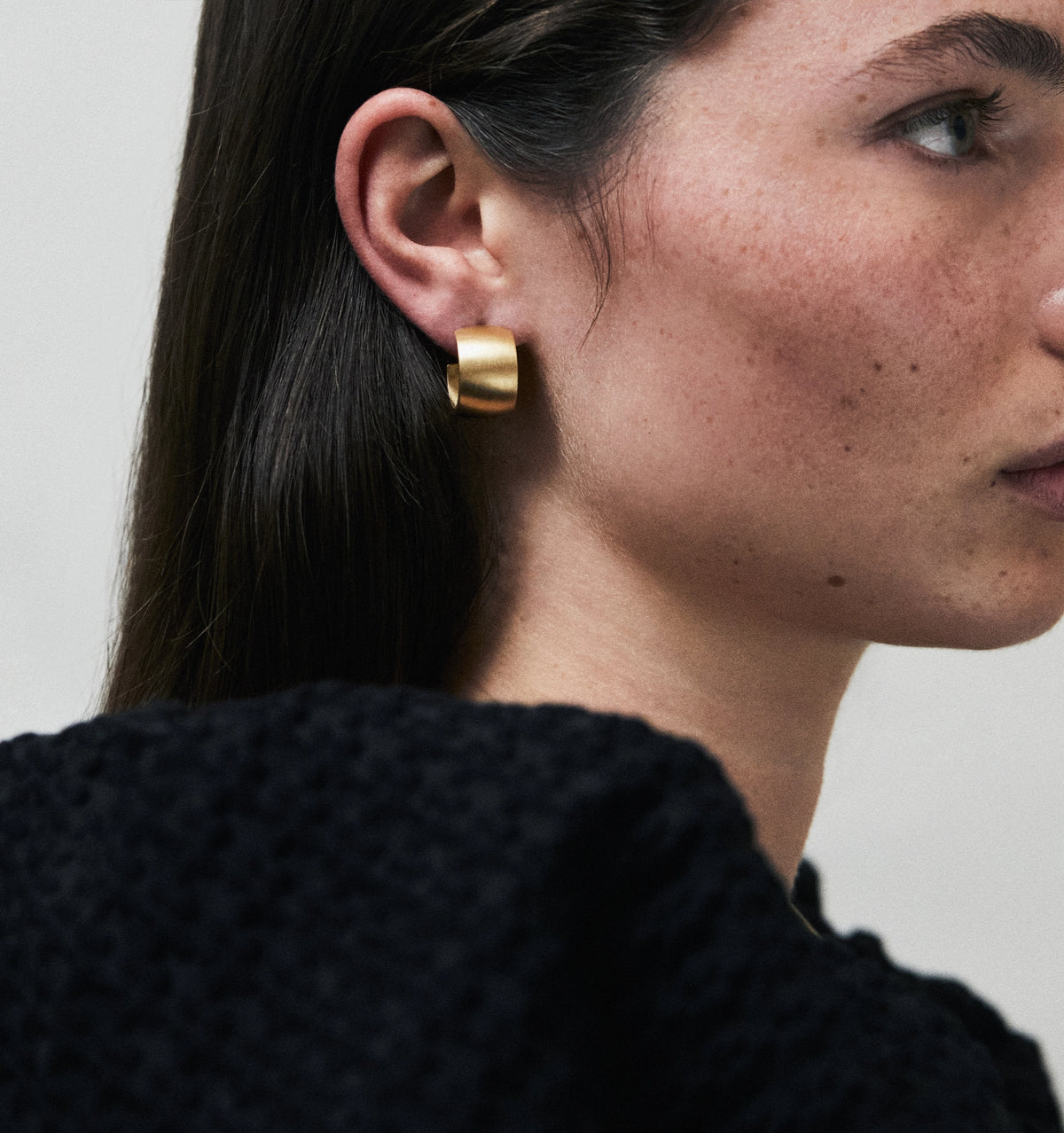 Woman wearing a gold sculptural earring against a neutral background.