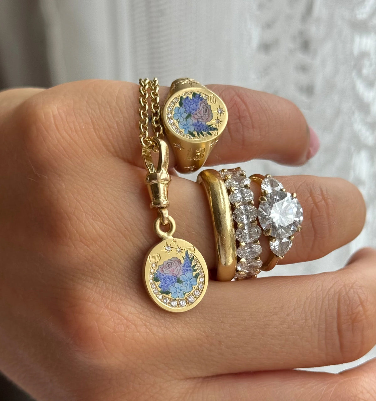 Woman wearing a gold charm necklace and multiple gold rings with engraved floral designs and diamonds.