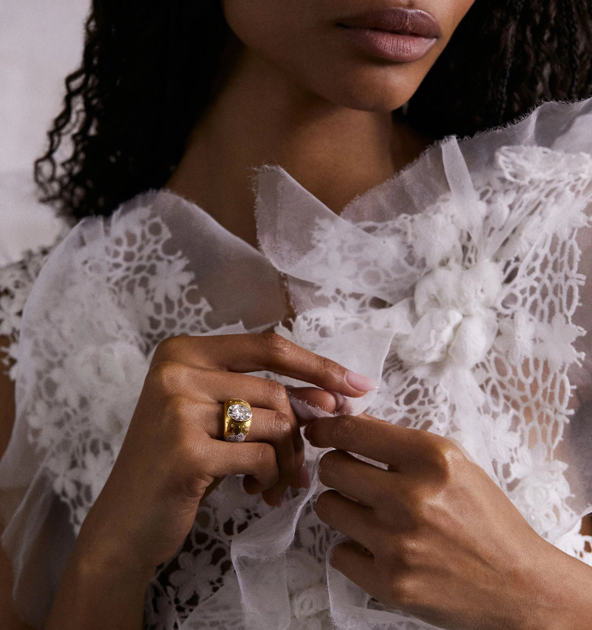 Woman wearing a gold ring with a large central stone and a smaller stone, dressed in a lace top.