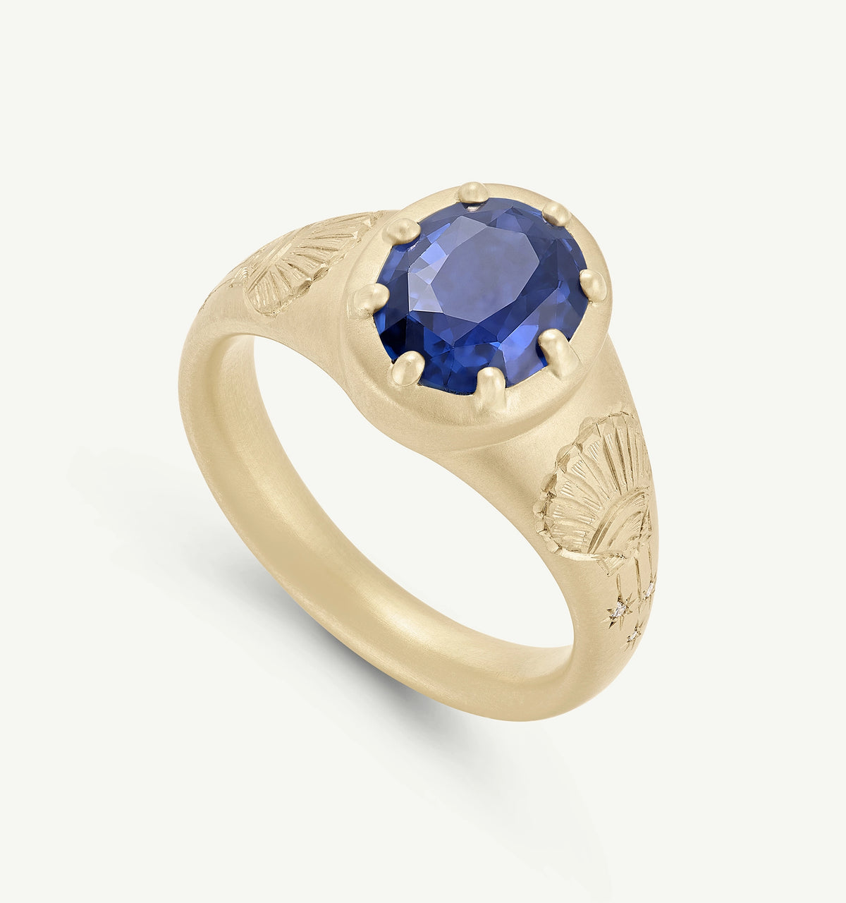 Gold ring featuring a large sapphire set in a textured band with engraved leaf motifs.