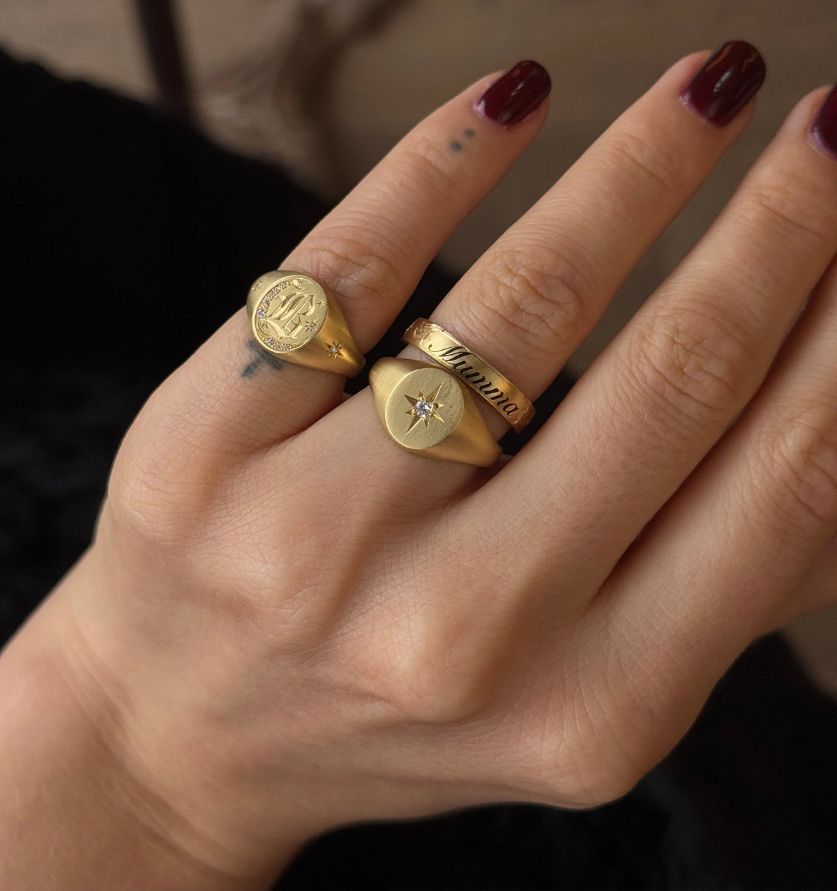 Woman wearing three gold rings: one engraved, one with a star-shaped diamond, and one with the name "Mamma."
