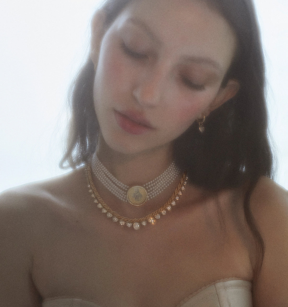 Woman wearing gold necklaces layered with pearl-like beads and a central gold pendant.