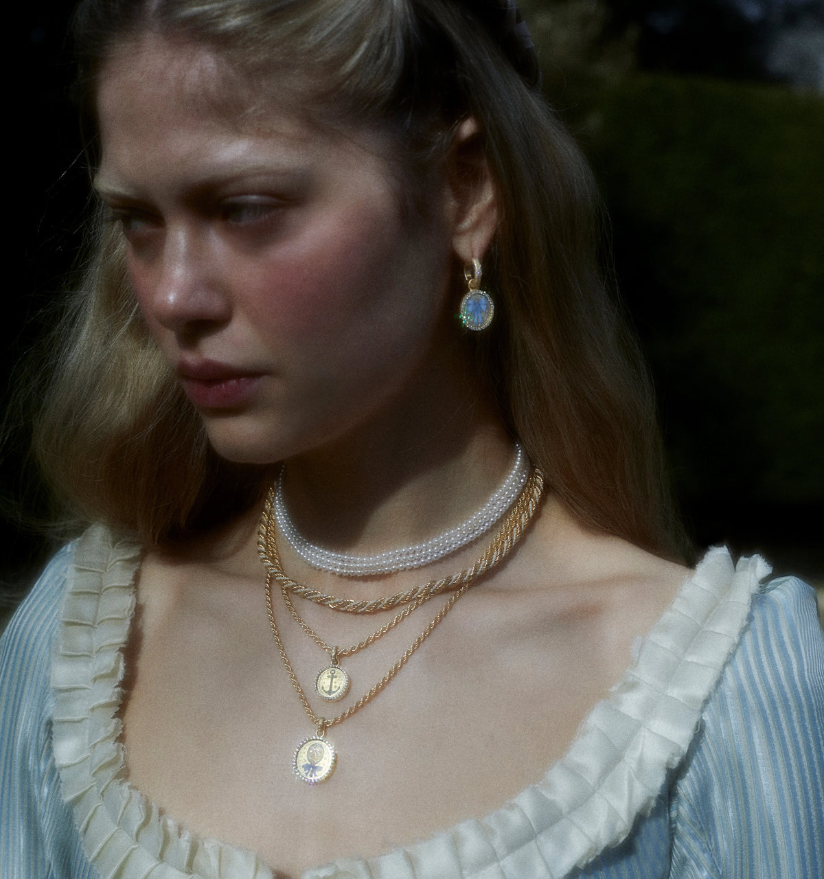 Woman wearing gold hoop earrings and layered gold necklaces with pendants, styled with a victorian-inspired outfit.