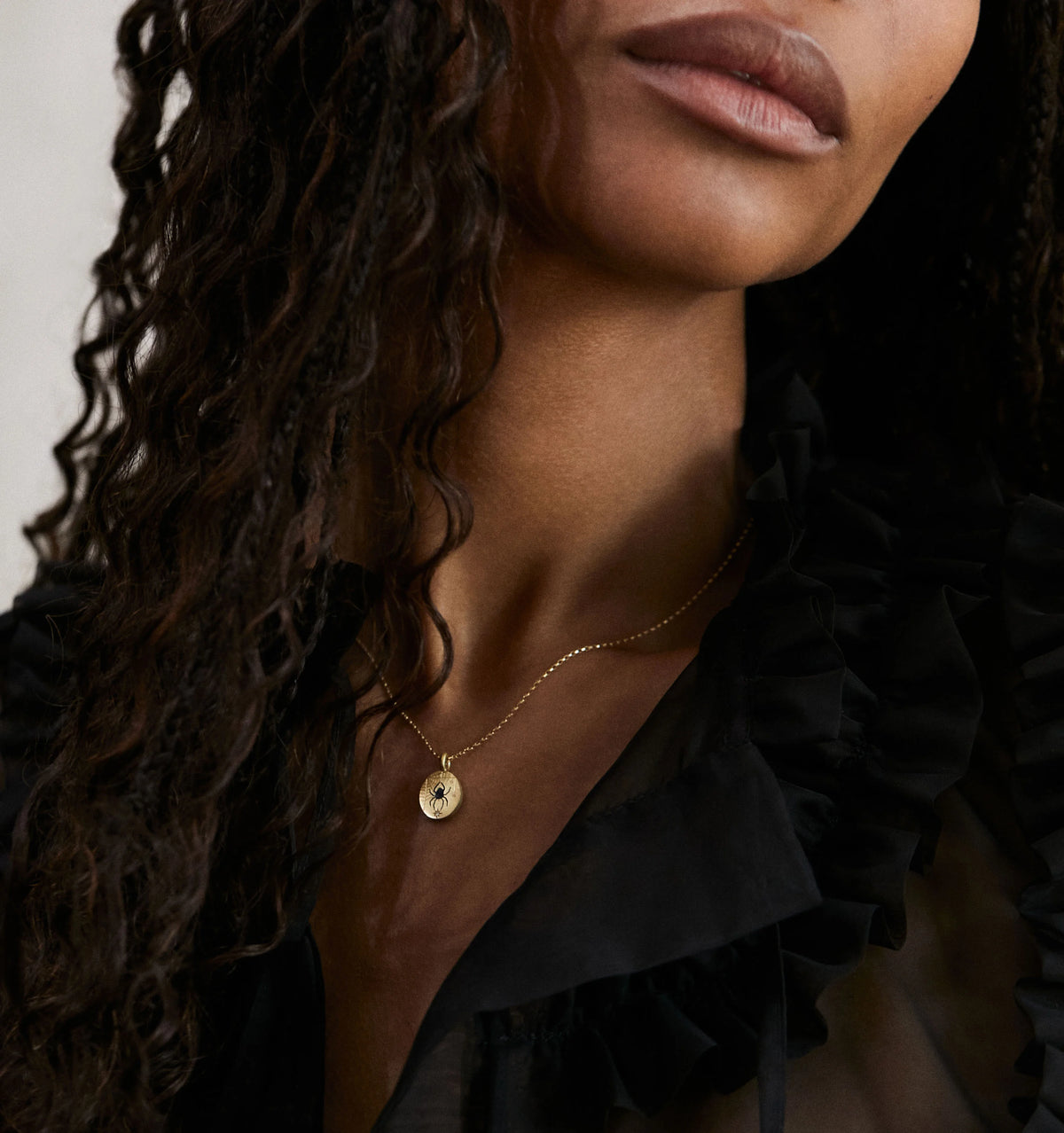 Woman wearing a gold necklace featuring a round pendant with a spider design.