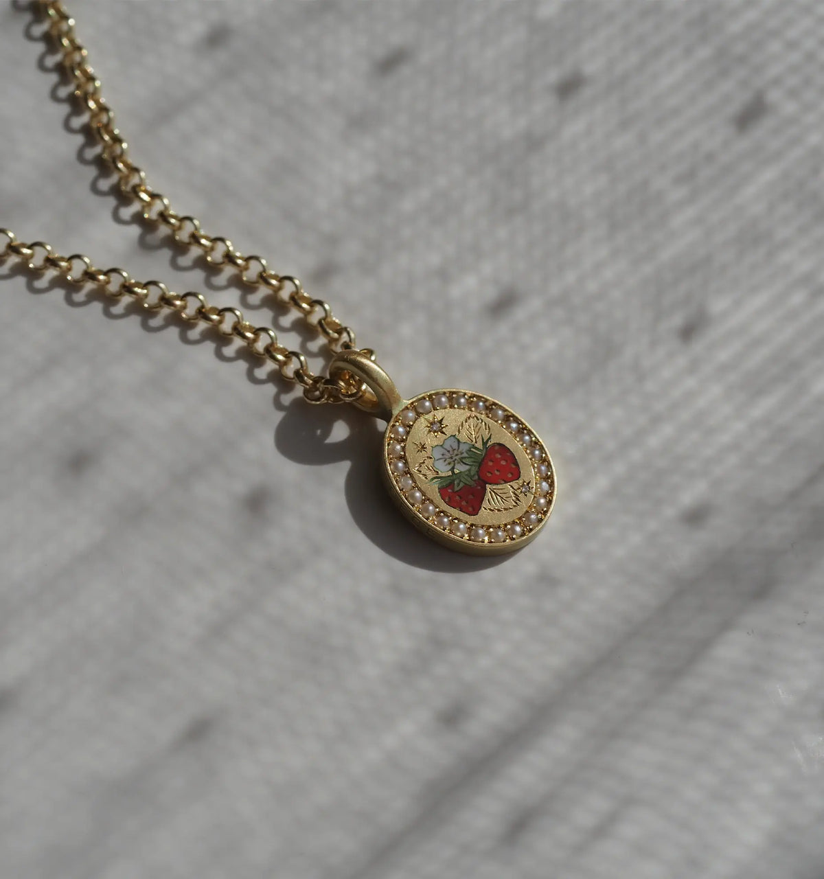 Gold necklace featuring an oval pendant with a strawberry and floral design in enamel, encircled by a beaded border.