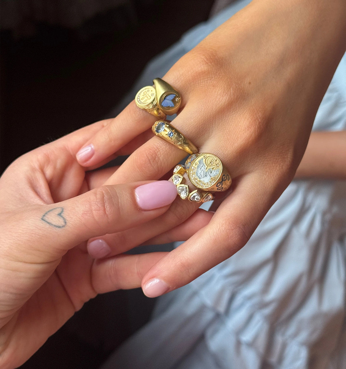 Woman wearing multiple gold rings, featuring a blue stone and engraved motifs.