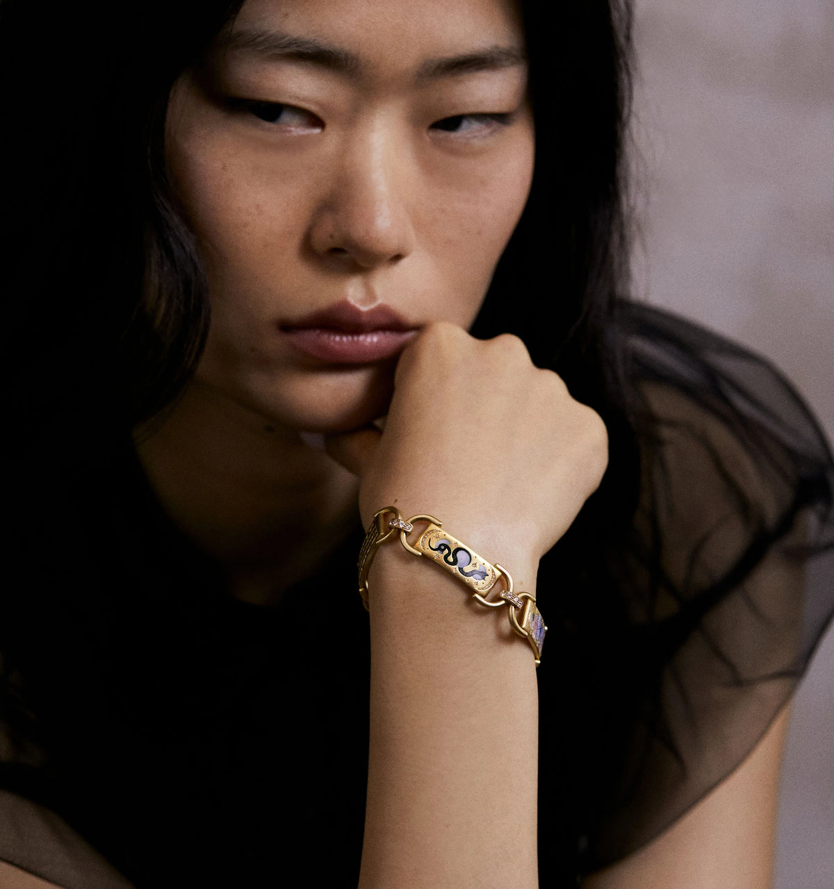 Woman wearing a gold bracelet featuring coloured enamel accents.
