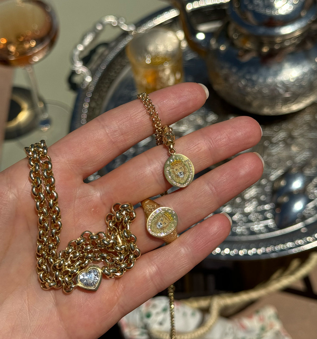 Woman wearing a gold chain necklace with a lion motif and a gold ring featuring a lion design, set against a decorative background.