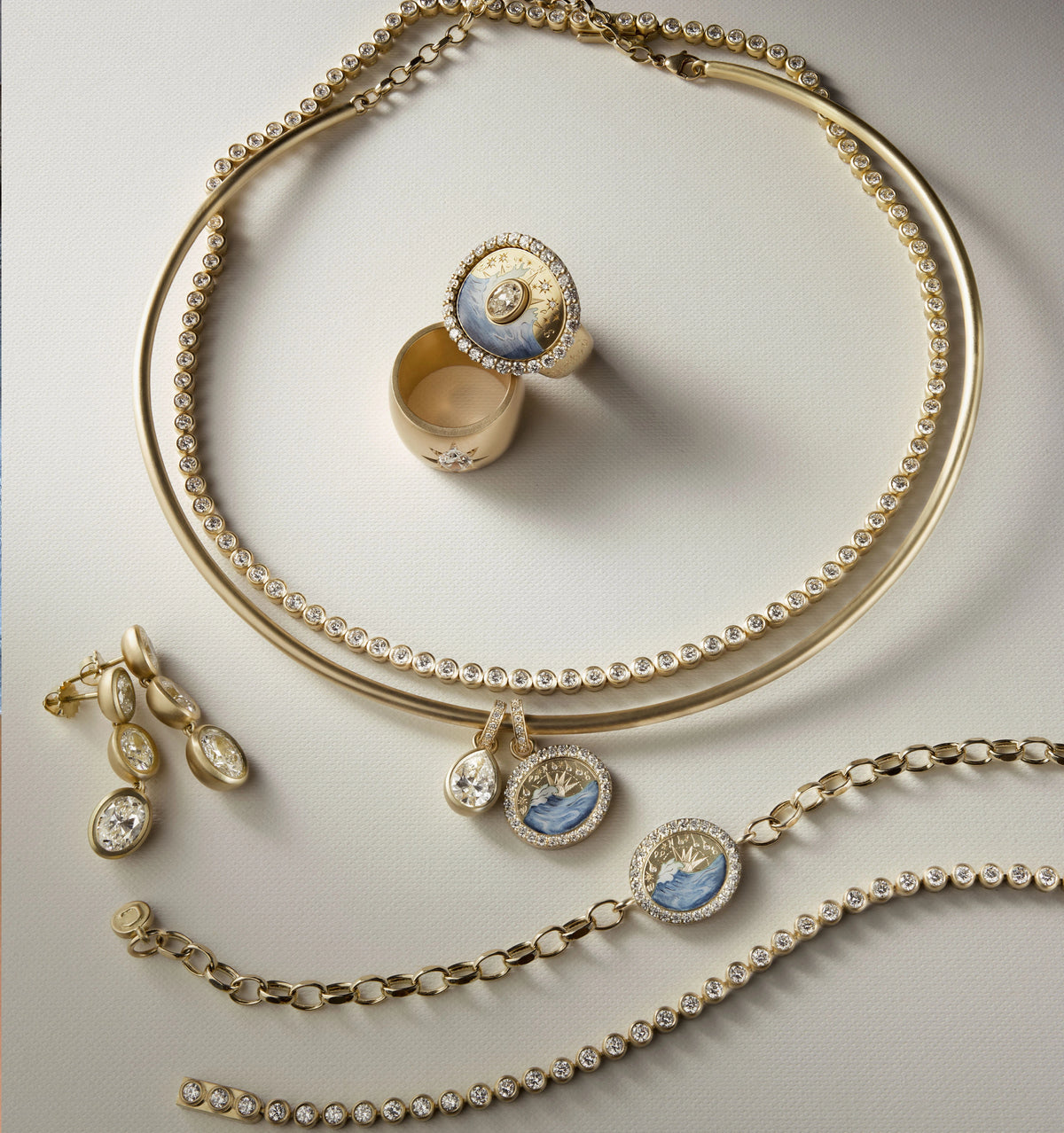 Gold necklace, bracelet, and earrings with defined settings, featuring blue enamel motifs and round stones. Gold ring with blue enamel and diamonds.