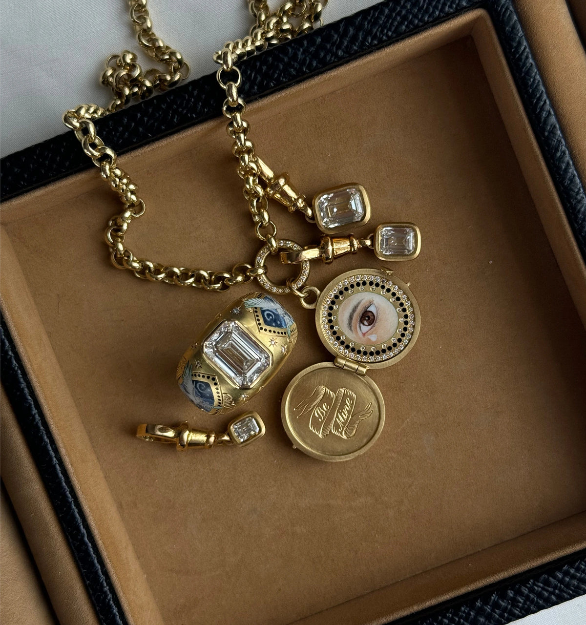 Gold necklace featuring a decorative pendant with a painted eye, multiple gold charms, and rectangular diamonds.