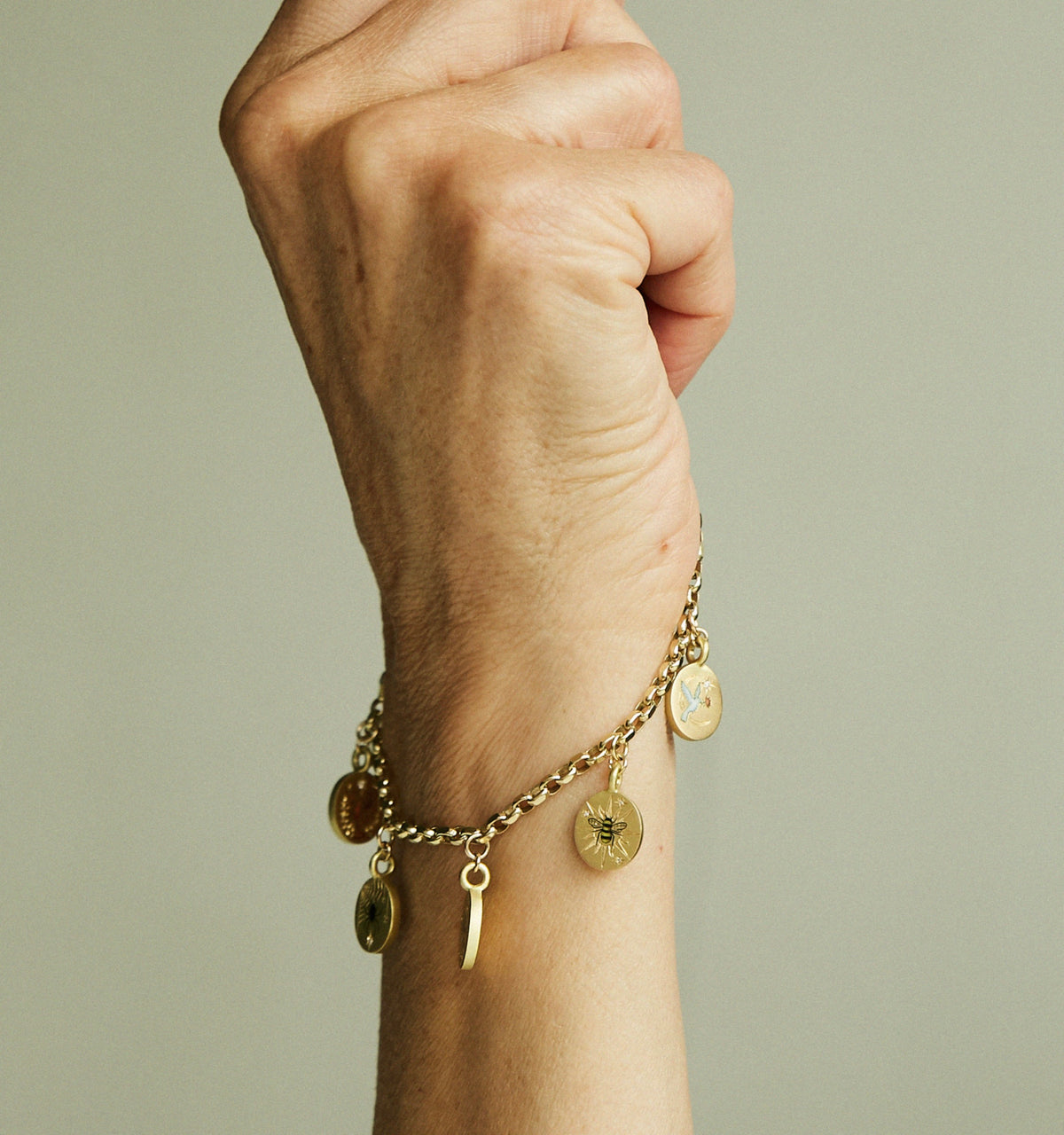 Woman wearing a gold charm bracelet with various engraved pendants on a neutral background.