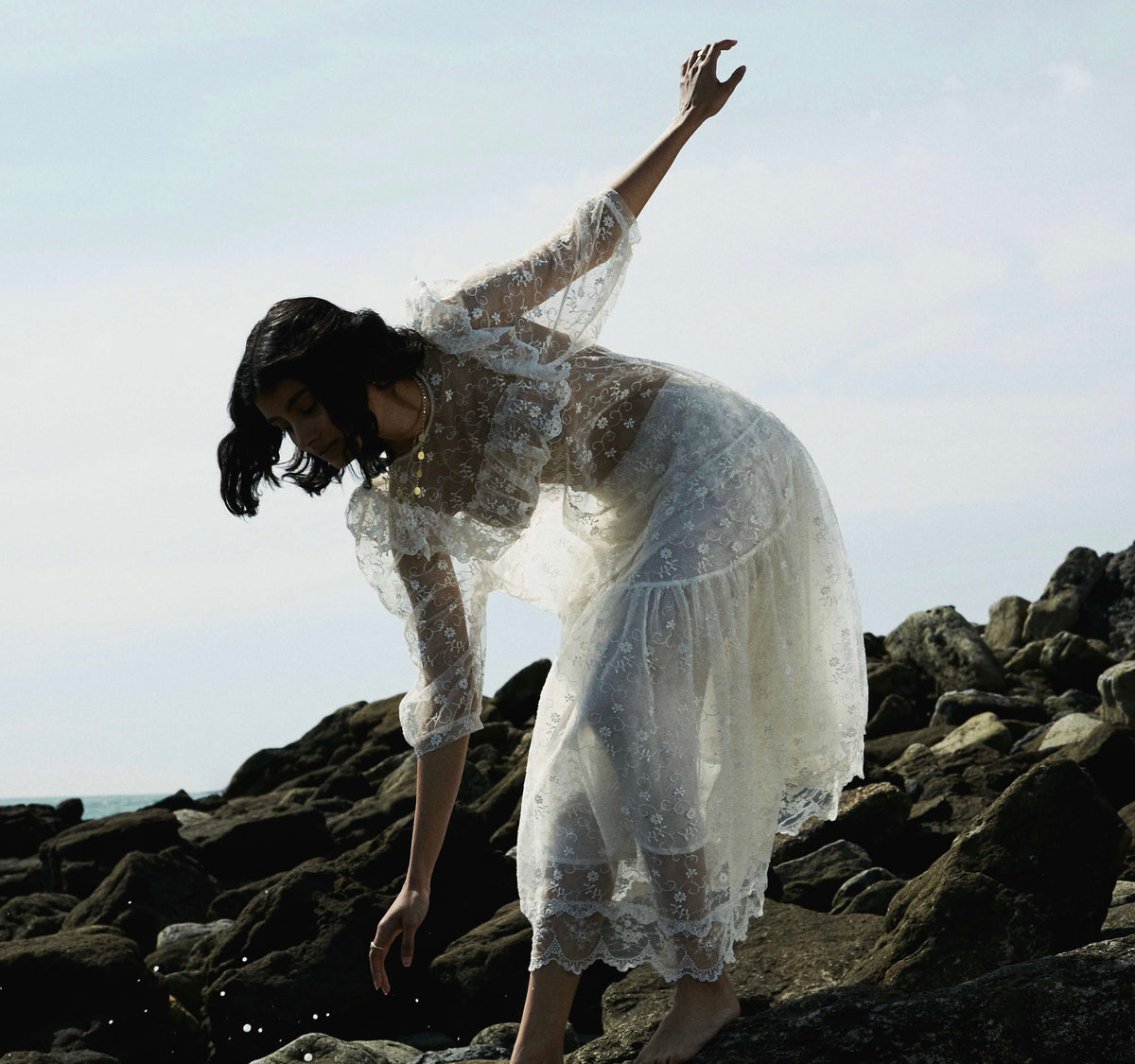 Woman wearing gold necklaces while standing on rocky beach.