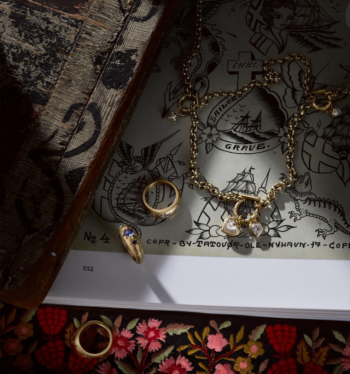 Gold necklace with heart-shaped diamond charms, styled with two gold rings set on a tattoo flash sheet.