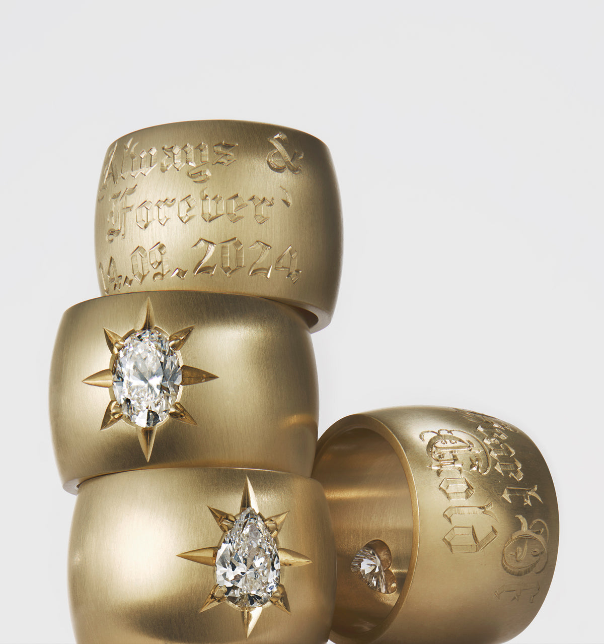 Gold rings featuring engraved messages and various-cut diamonds, stacked on a white background.