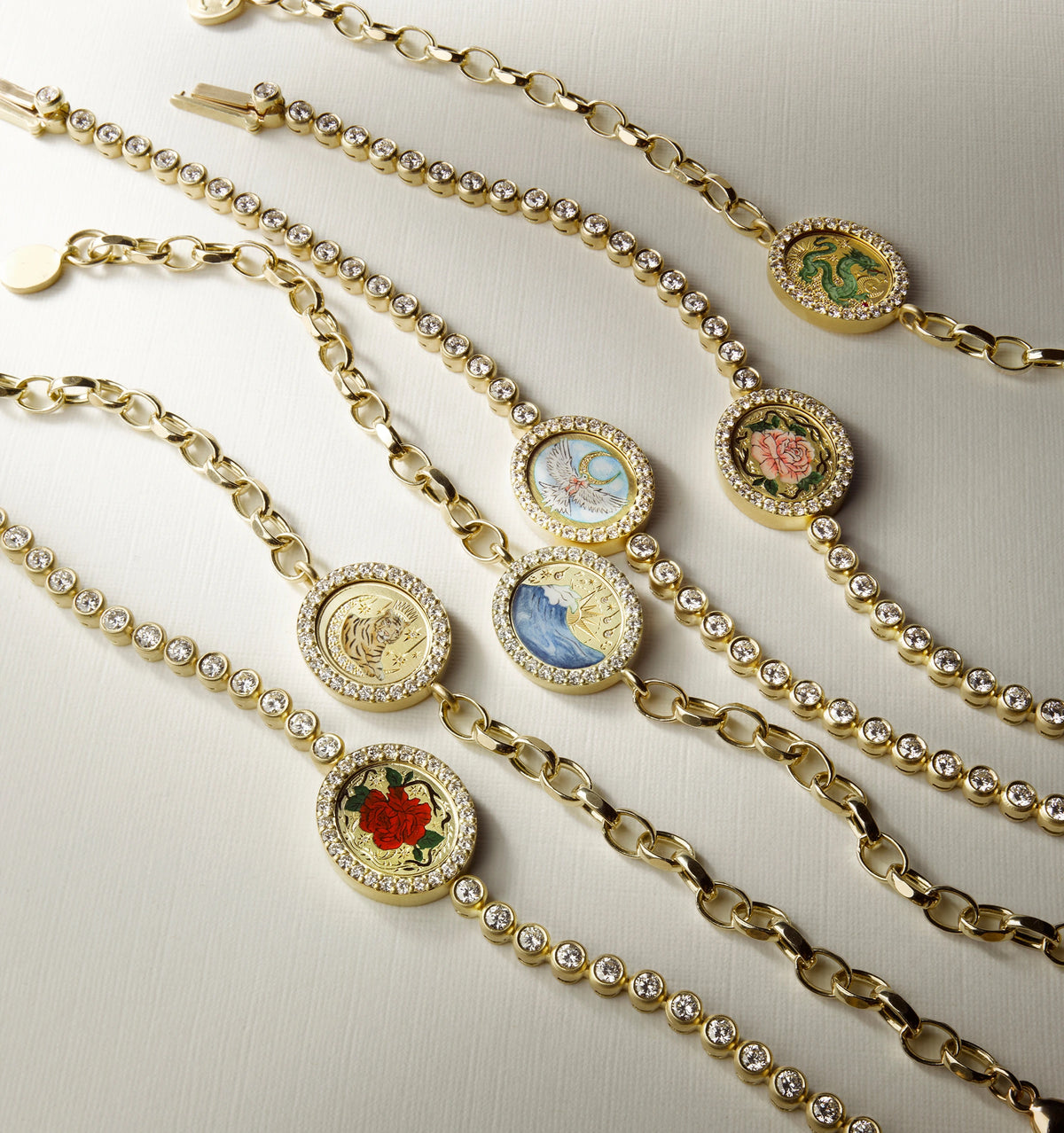 Gold bracelets featuring enamel motifs and accented with circular diamonds on a light surface.