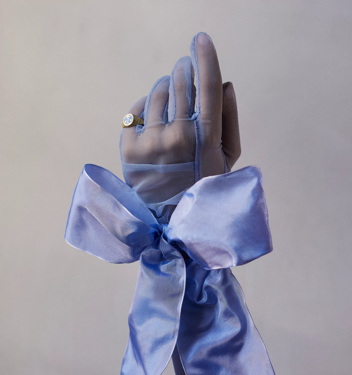 Woman wearing a gold ring with a round diamond on a hand adorned with a light blue sheer glove and bow.