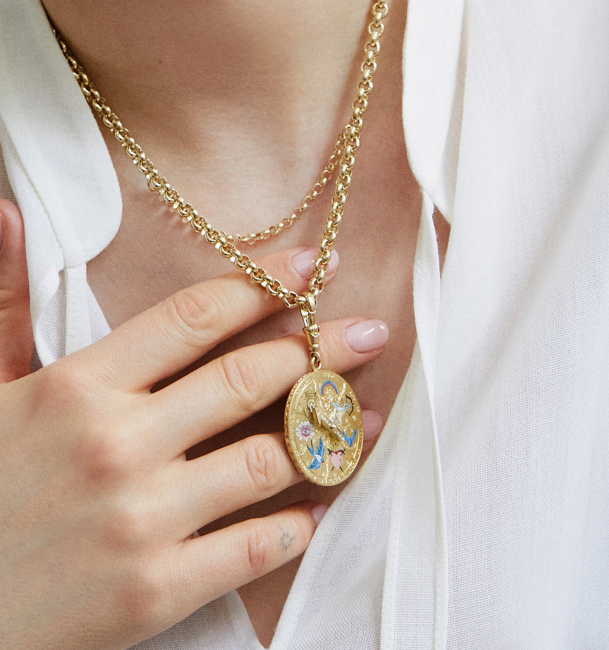 Woman wearing a gold chain necklace with an oval pendant featuring flowers in enamel.