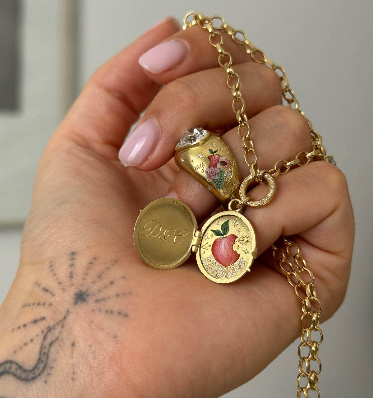 Woman wearing a gold locket necklace and a gold ring with a floral design.
