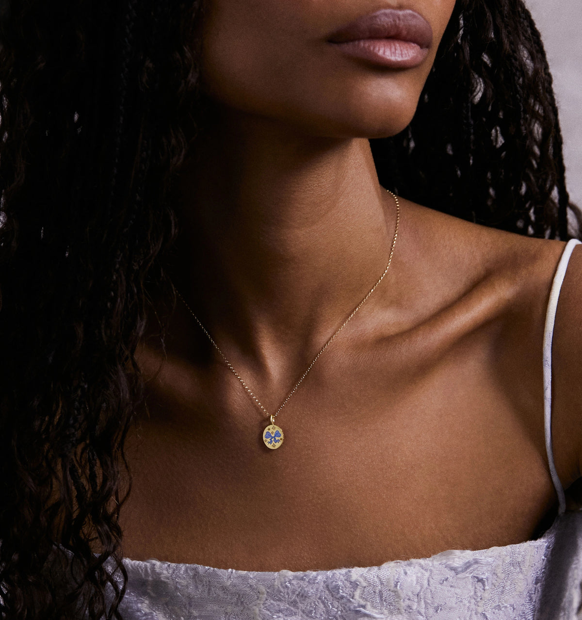 Woman wearing a gold necklace with an enamel floral pendant.