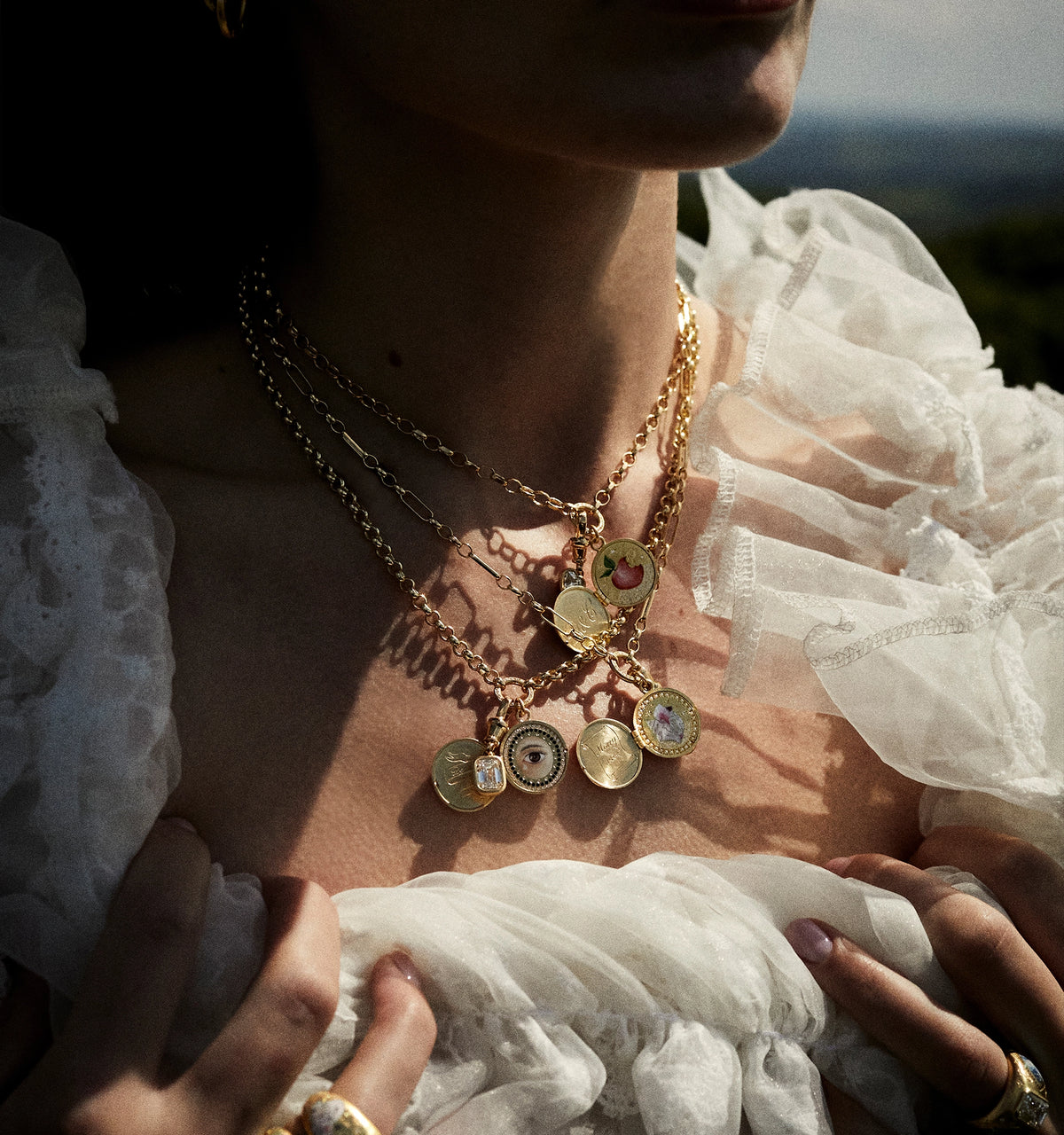 Woman wearing multiple gold necklaces featuring enamel details and pendants.