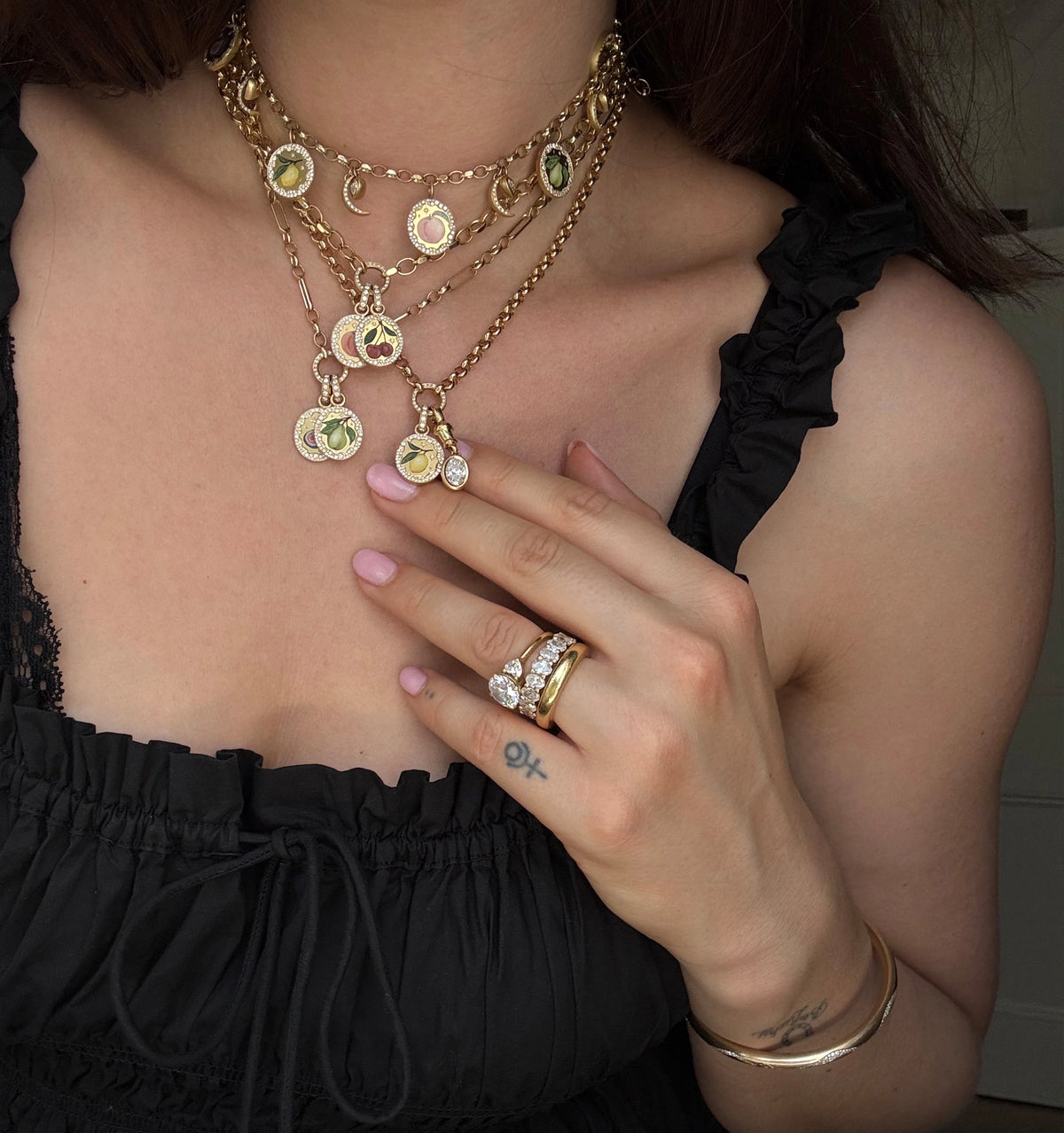 Woman wearing layered gold necklaces with colourful enamel pendants and a gold ring with diamonds.