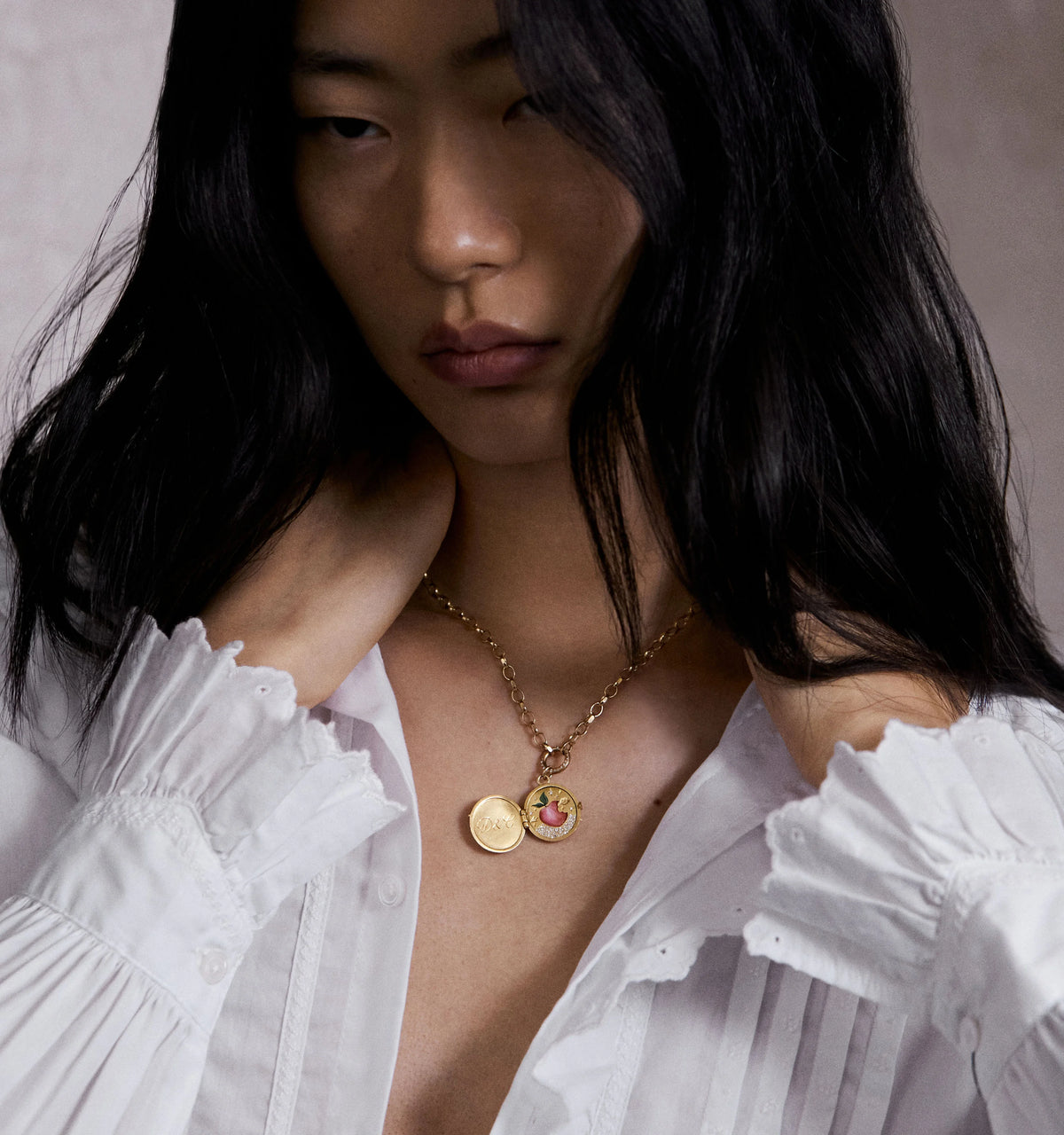 Woman wearing a gold necklace featuring a round pendant with a pink motif and an engraved coin charm.